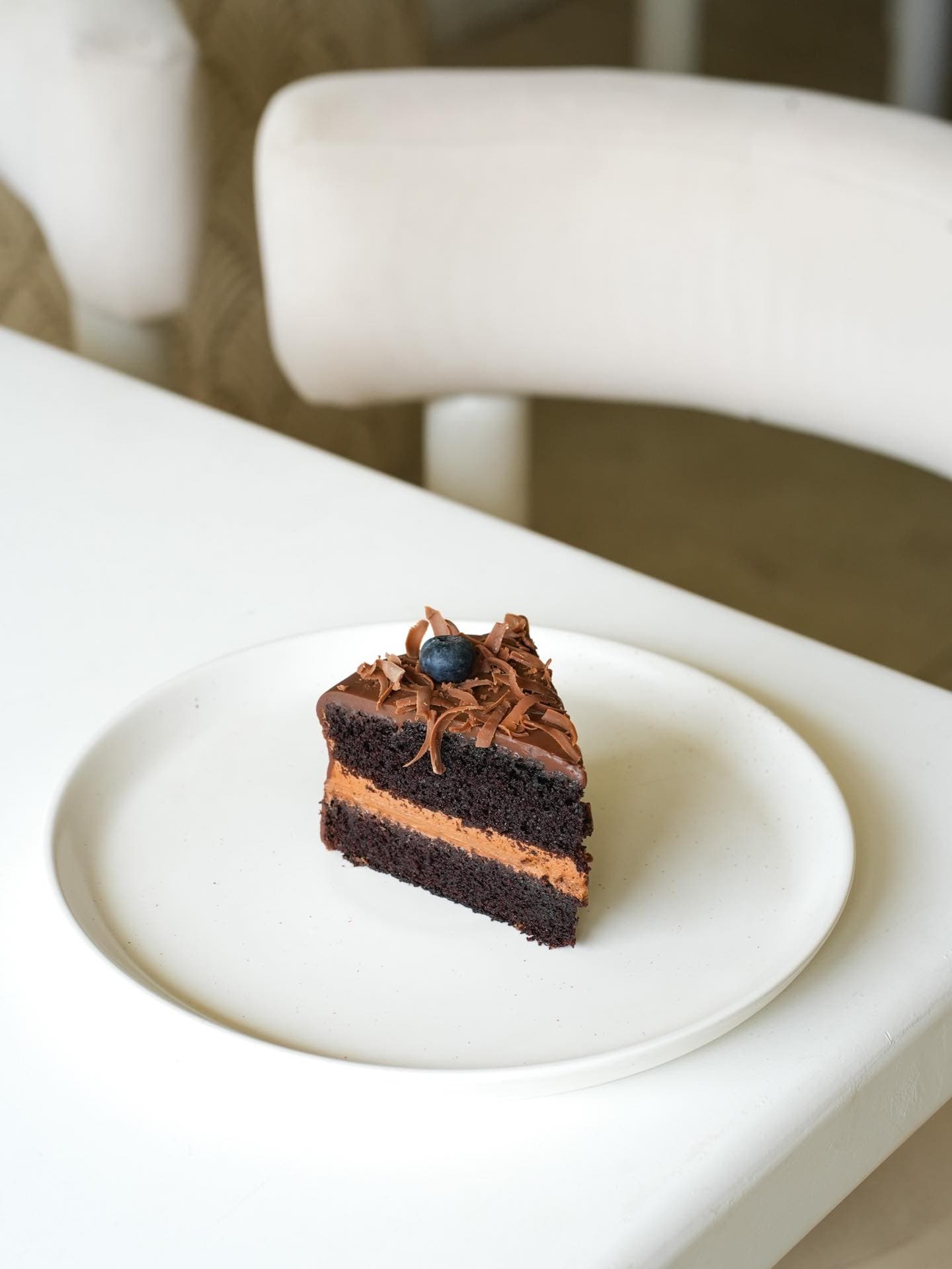 A wedge of dark chocolate cake with chocolate shavings and a blueberry on top