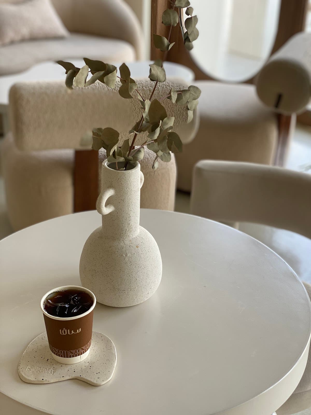A speckled ceramic vase with dried eucalyptus and a SAVVA cold brew on the lounge table