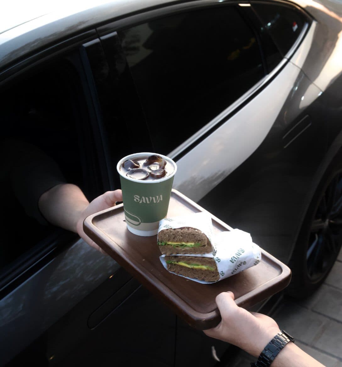 A SAVVA tray with coffee and a sandwich handed out to a car window